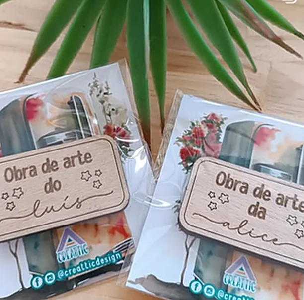 Duas placas de madeira gravadas com o texto obra de arte e o nome de uma criança, em embalagens com o logótipo Creattic.